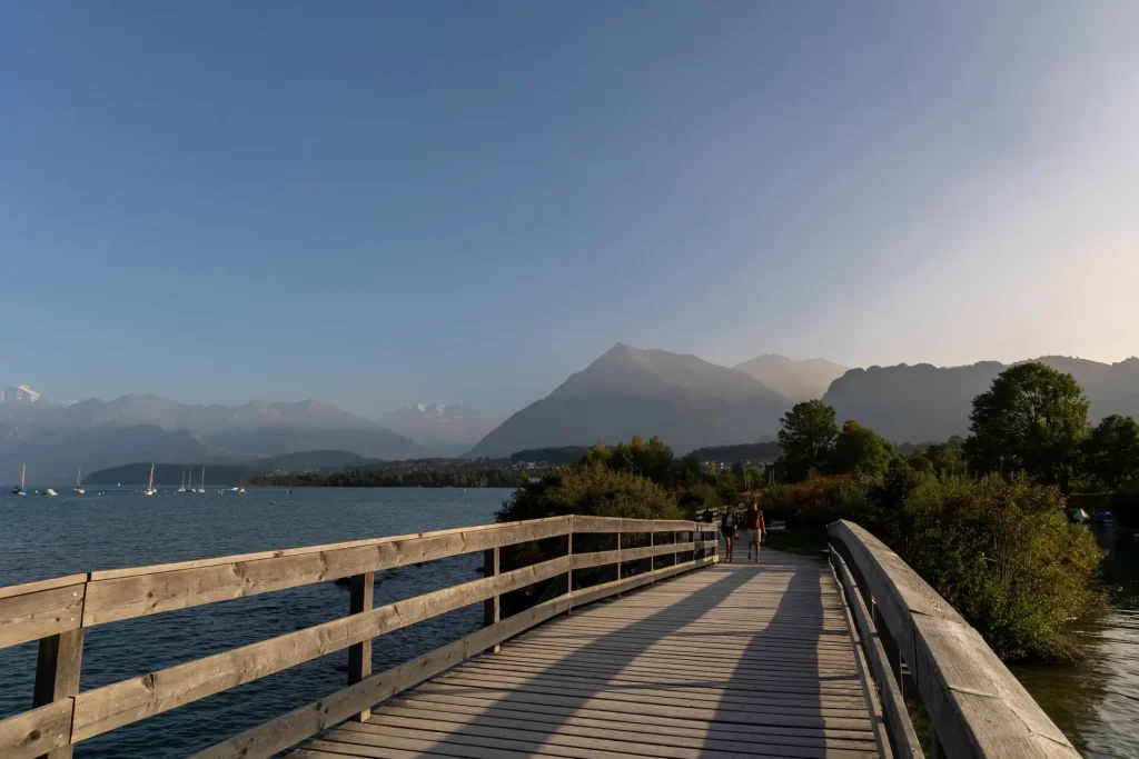 Holzsteg am Seeufer, links der Thunersee mit Segelbooten, dahinter die Berge.